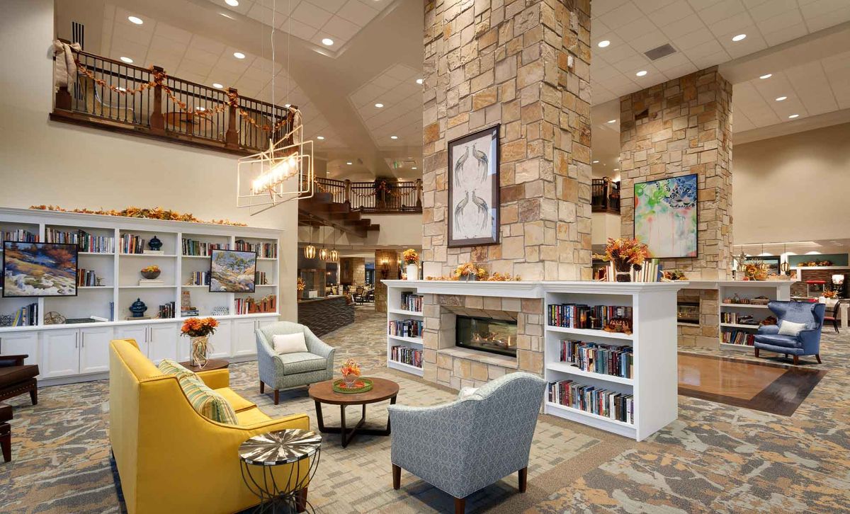 A cozy lobby area with modern decor, featuring a stone fireplace, comfortable seating, and bookshelves.