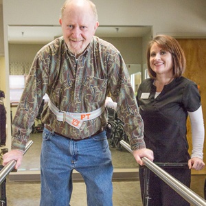 A patient engages in a physical therapy session using walking bars, supported by a healthcare professional.