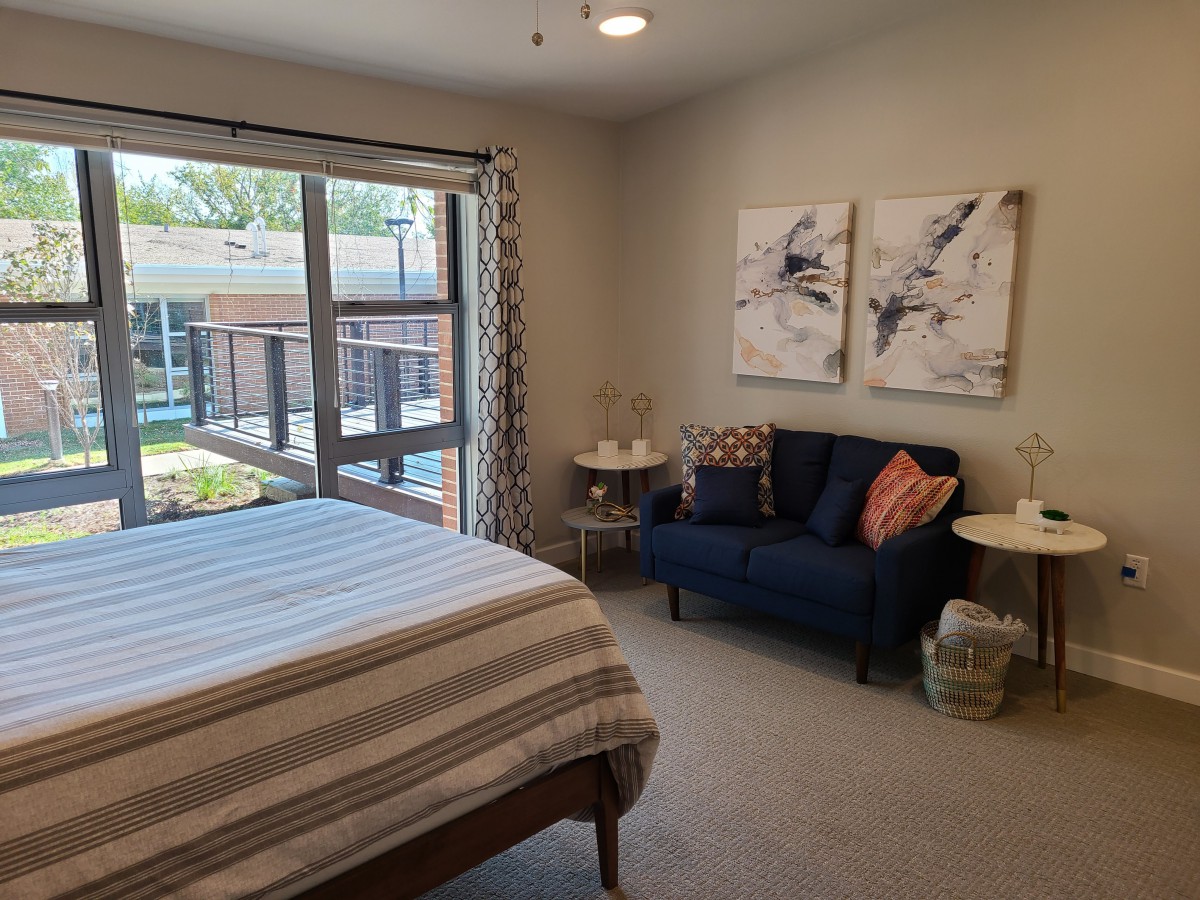 A cozy bedroom with a bed and seating area near a large window, featuring abstract artwork on the wall.