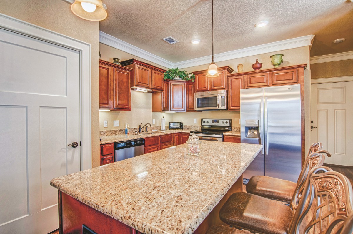 A modern kitchen with wooden cabinets, a granite countertop island, and sleek appliances.