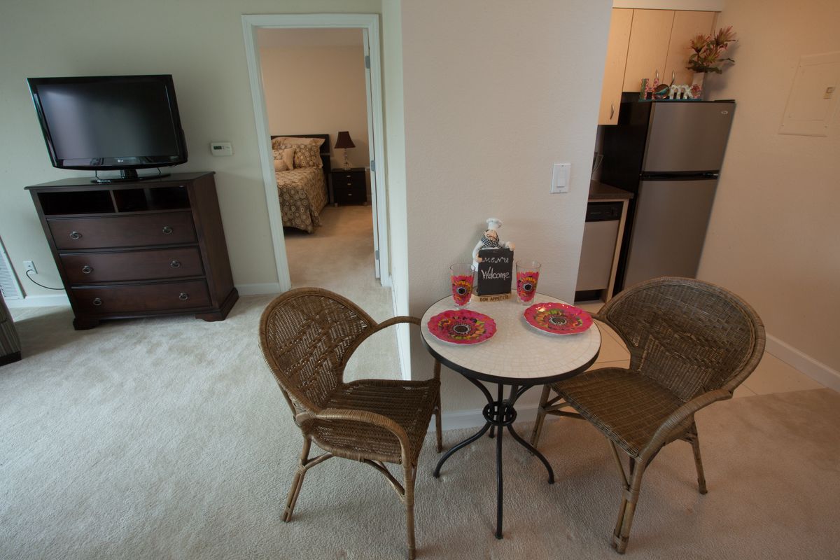 A cozy apartment interior featuring a small dining area with a round table and chairs, adjacent to a kitchen and bedroom.