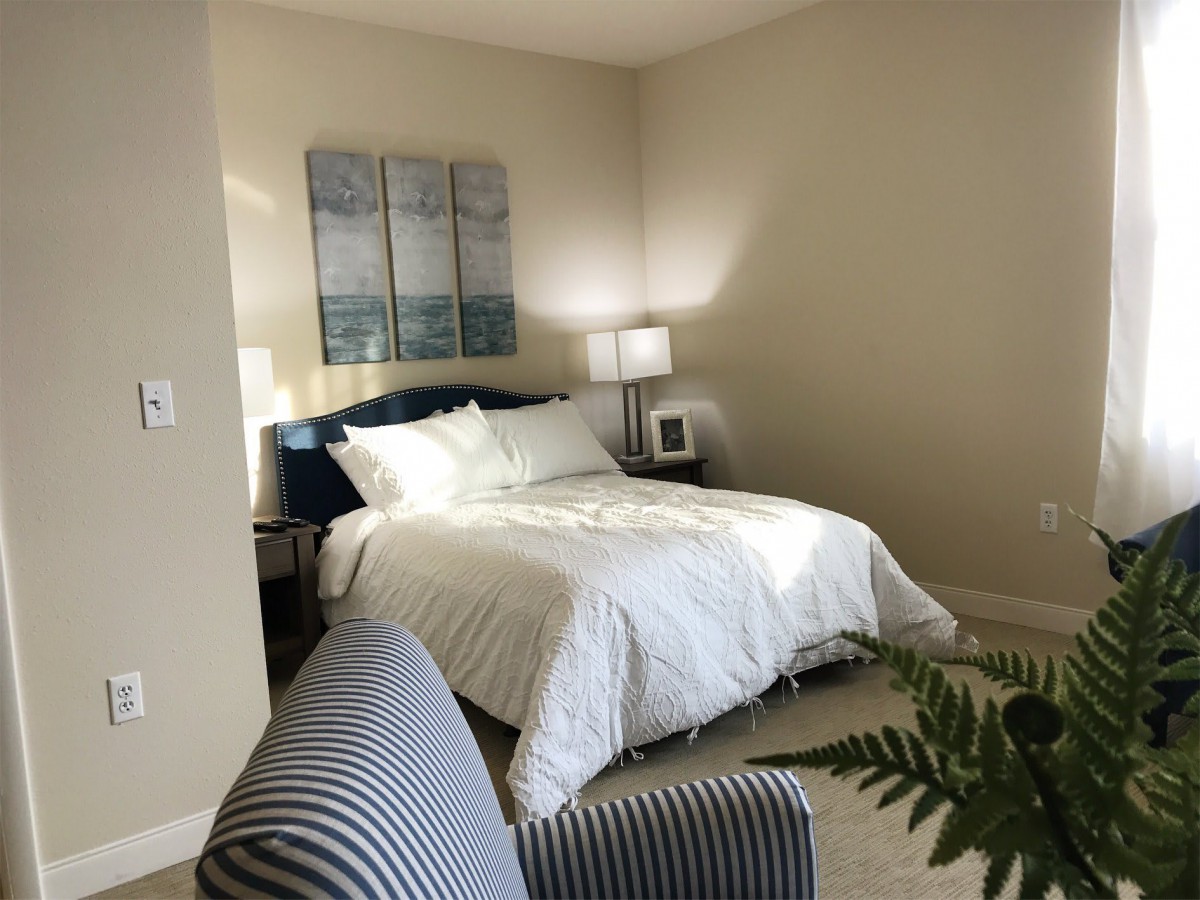 A cozy bedroom with a neatly made bed, bedside tables, lamps, and decorative artwork.