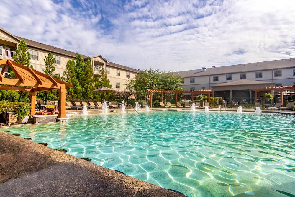 A scenic view of a hotel resort with a large outdoor swimming pool and fountains, set against a clear sky.