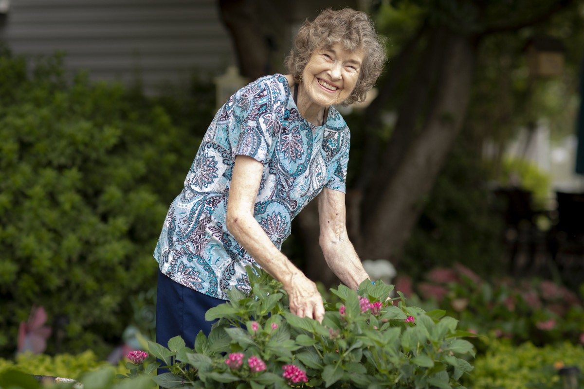 An elderly woman smiling while tending to her garden.