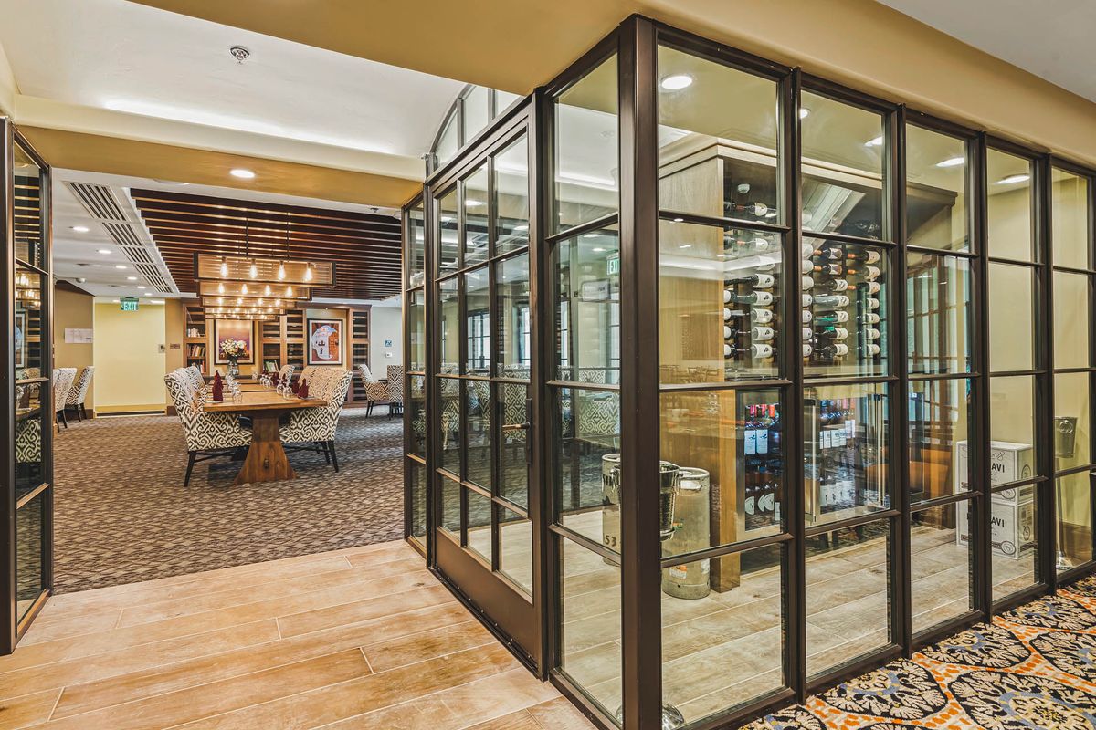 A modern restaurant interior featuring a glass-enclosed wine cellar and seating area.