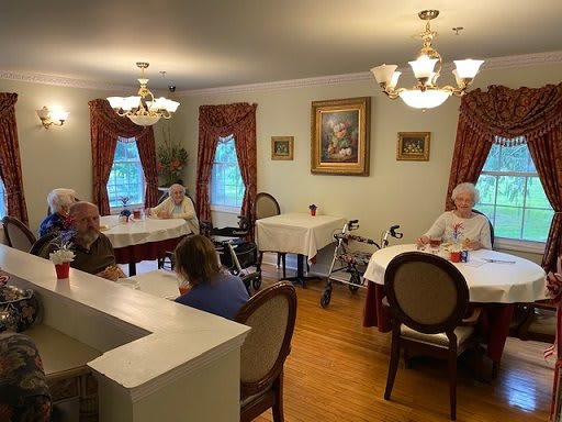 A cozy dining room with seniors seated at tables, adorned with elegant chandeliers and red curtains.