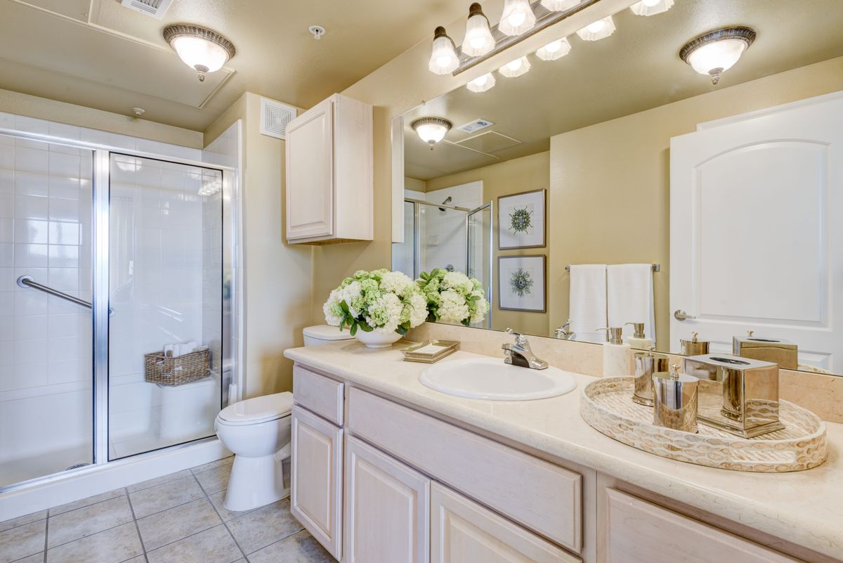 A modern bathroom with a large mirror, double sink, and shower area adorned with decorative flowers and towels.