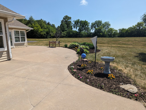 A serene outdoor patio area featuring a well-kept garden, birdbath, and open field in the background.