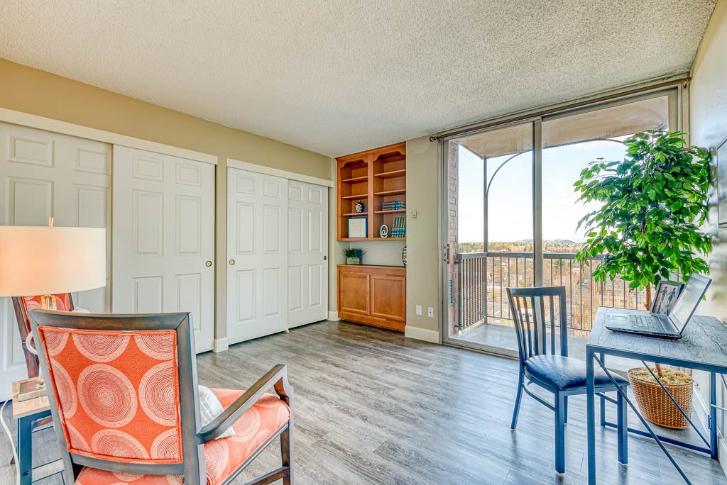 A bright living room with hardwood flooring, featuring a chair, bookshelf, and a balcony view.