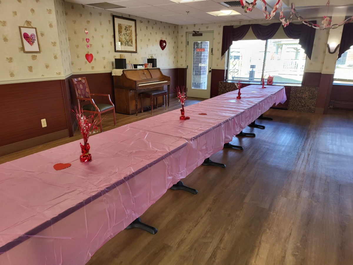 A long table with pink decorations set up for a Valentine's Day celebration in an interior room.