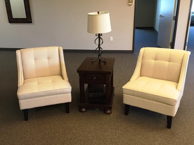 A cozy setup with two beige chairs, a wooden side table, and a decorative lamp.