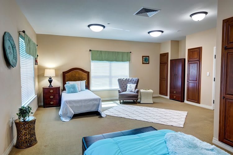 A cozy bedroom with two beds, a comfortable chair, and a window with green curtains.