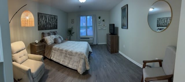 A cozy bedroom with a neatly made bed, wooden flooring, and a television on a dresser.