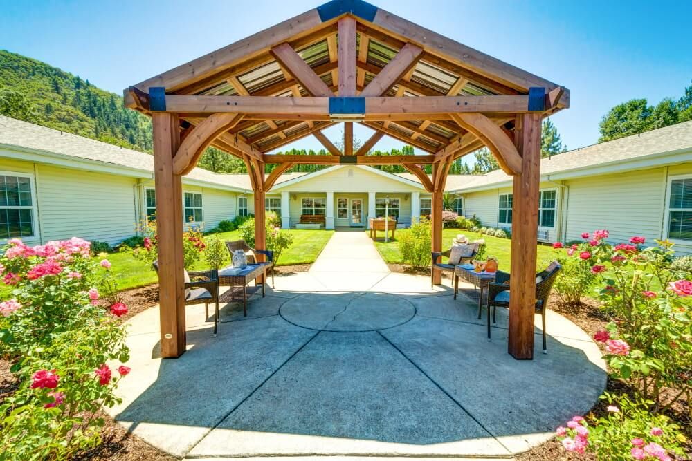 A scenic outdoor area featuring a wooden gazebo, surrounded by benches and landscaped gardens.