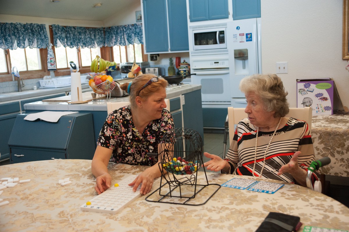 Two senior women engaged in a conversation at a kitchen table.