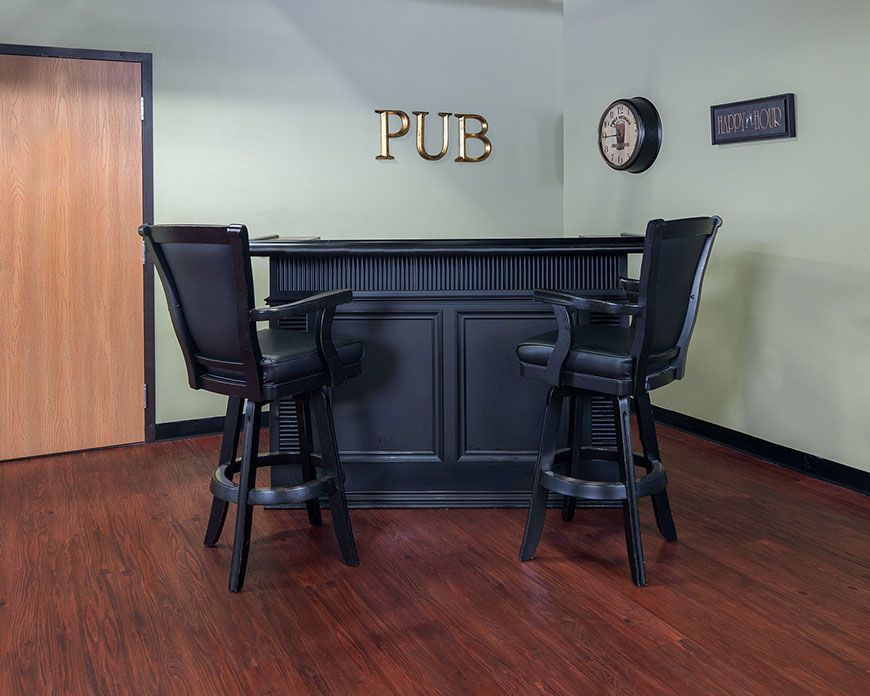 A small pub setup with a black counter and matching chairs in a room with wooden flooring.