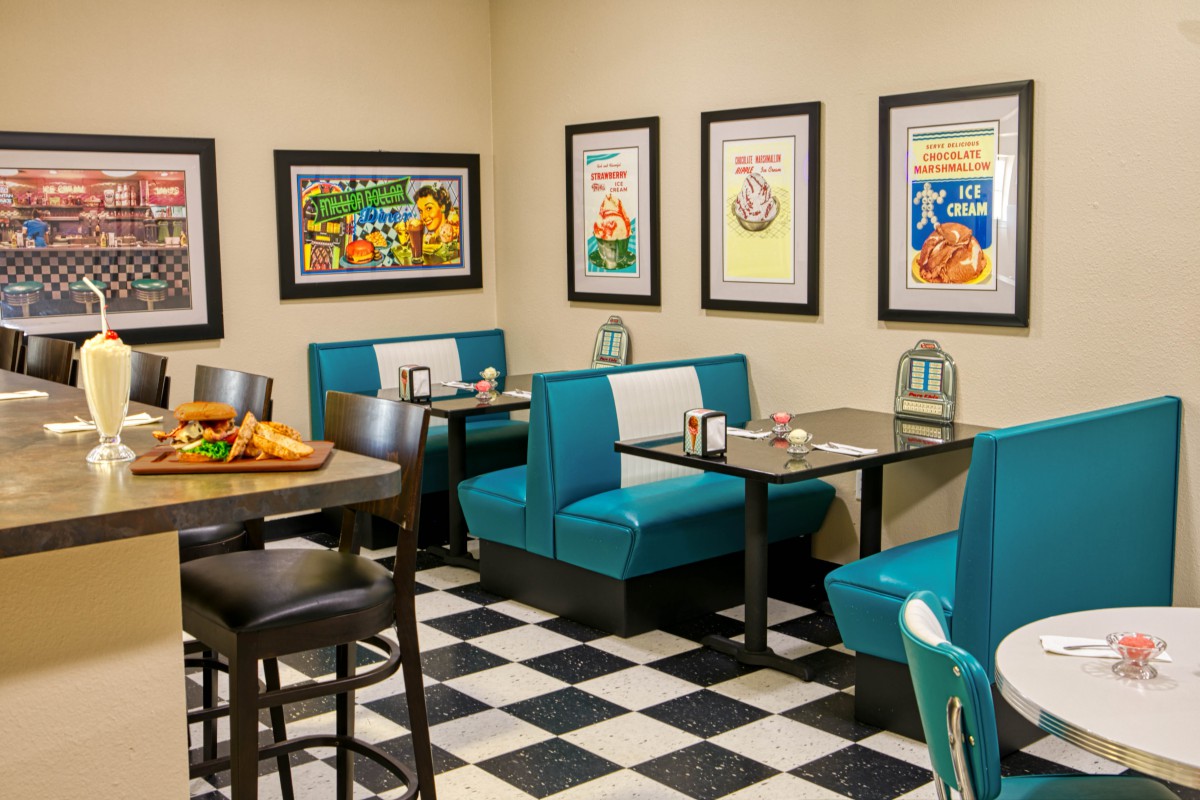 A retro-style diner with teal booths and checkered flooring, featuring vintage posters on the walls.