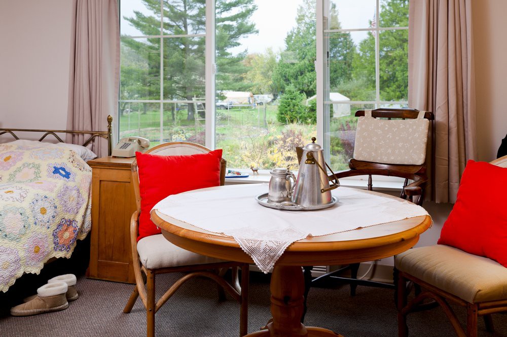 A cozy dining area with a round table and chairs, featuring a tea set, situated near a large window with a scenic outdoor view.