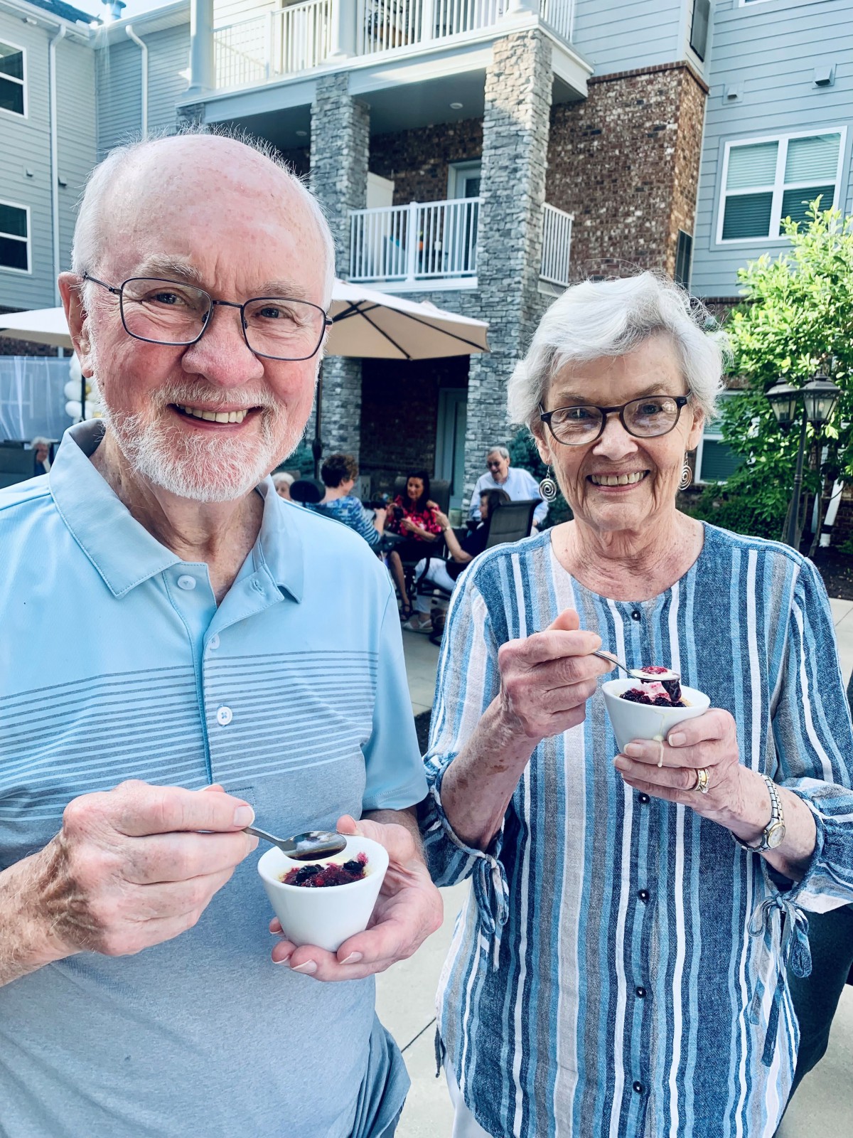 An elderly couple enjoying dessert outdoors on a sunny day.