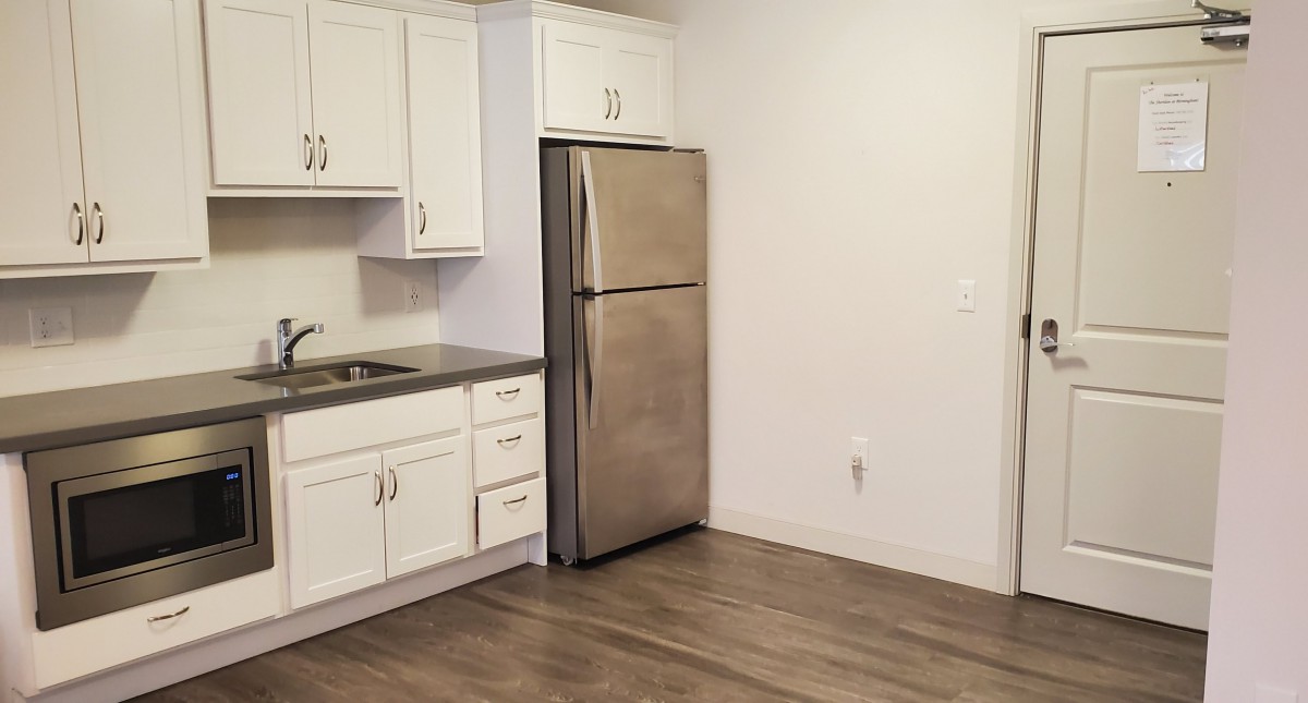 A modern kitchen featuring white cabinets, stainless steel refrigerator, and wood flooring.