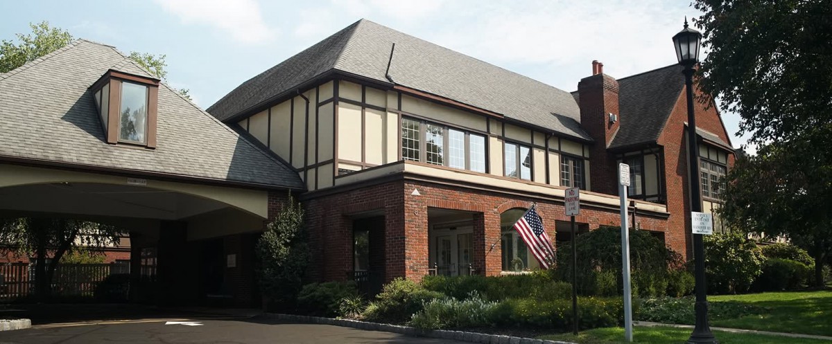 A traditional Tudor-style building with an American flag beside a landscaped garden.