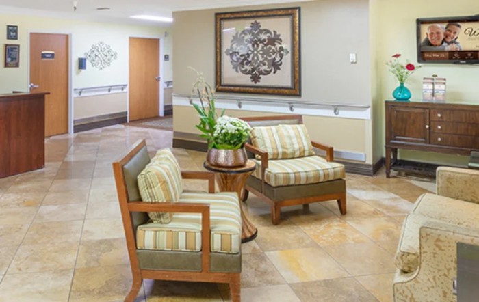 A cozy waiting area featuring two cushioned chairs and a small table with a potted plant, set against a warmly decorated wall.