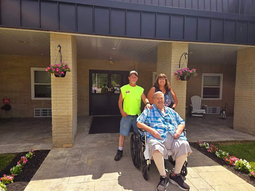 A joyful family moment captured on the porch with a grandparent in a wheelchair, flanked by two young family members.