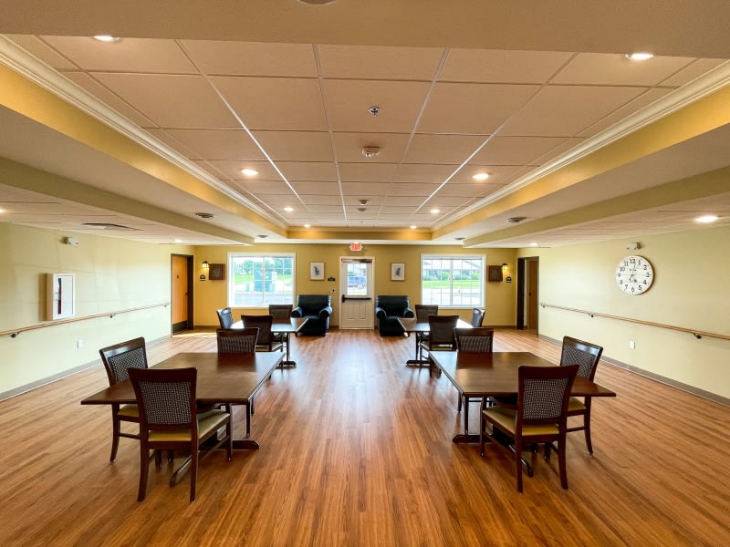 An empty dining room with wooden floors, arranged tables and chairs, and large windows.