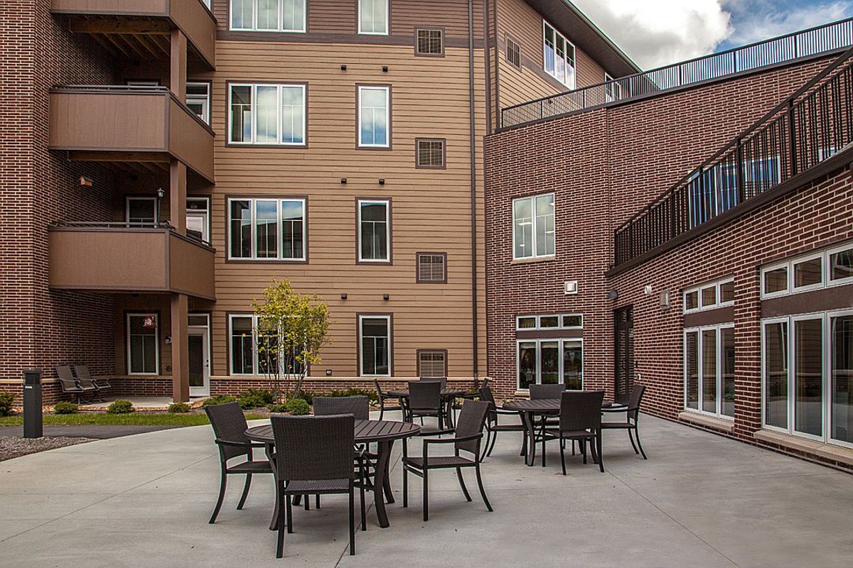 A courtyard with outdoor tables and chairs in front of a brick apartment building.