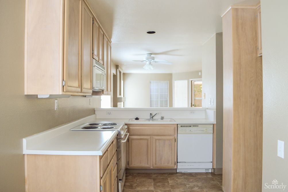 A modern kitchen with wood cabinets and white countertops, featuring natural light and neutral colors.