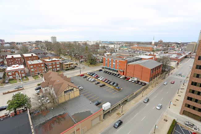 Aerial view of a city scene featuring buildings, a parking lot, and a street with vehicles.