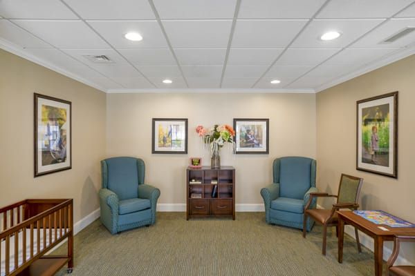 A cozy waiting room with blue armchairs, artwork on the walls, and a small table adorned with flowers.