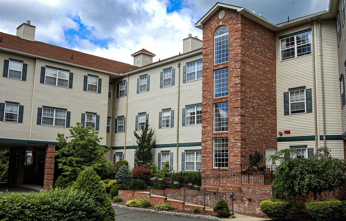 A residential building with brick and siding exterior, surrounded by gardens.