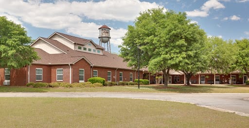 A brick building with a water tower in the background, surrounded by trees and a cloudy sky.