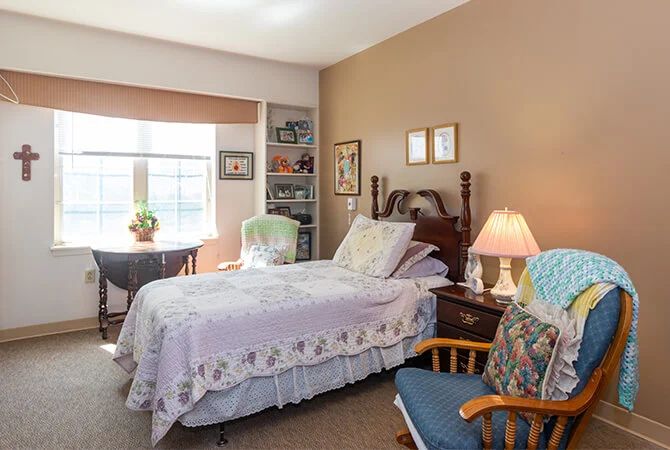 A cozy bedroom with a single bed, a bedside table with a lamp, and a comfortable chair by the window.