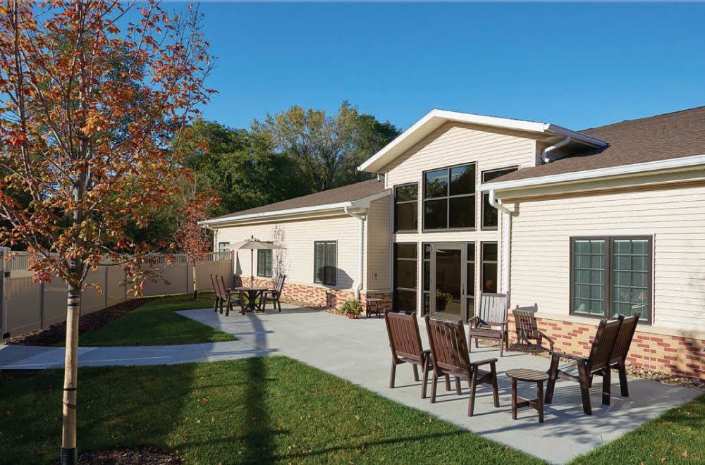 A modern building with a patio area featuring outdoor seating, surrounded by grass and autumn trees.