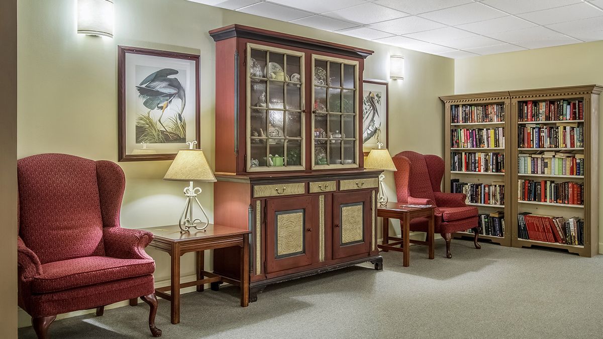 A traditional interior space featuring a wooden cabinet, bookshelves, armchairs, and decorative artwork.