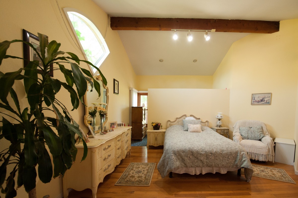 A cozy bedroom with elegant furniture, wooden floors, and decorative plants.
