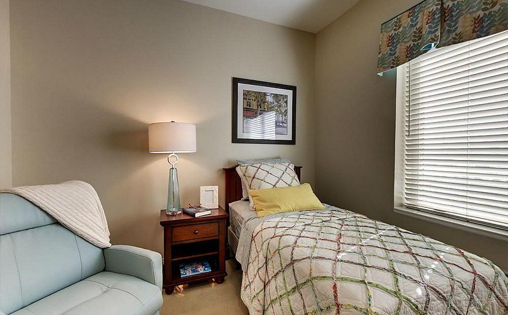 A cozy bedroom with a single bed, nightstand, and chair.