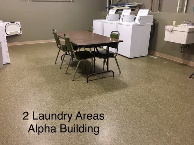 Laundry area with washing machines and a table with chairs in the Alpha Building.