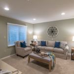 A cozy living room featuring a sofa, armchair, and a coffee table, decorated with lamps and a wall clock.
