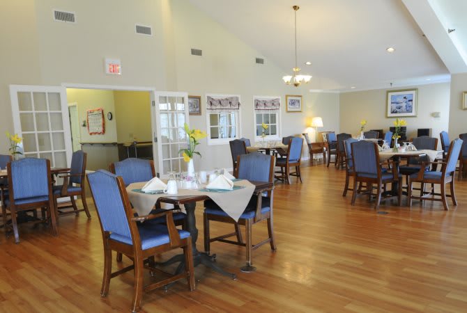 A cozy dining room with neatly arranged tables and blue cushioned chairs, featuring warm lighting and wooden floors.