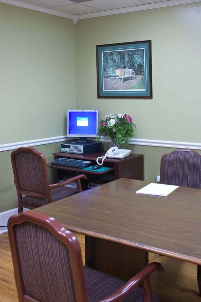 A small office meeting room with a desk, computer, chairs, and a telephone.