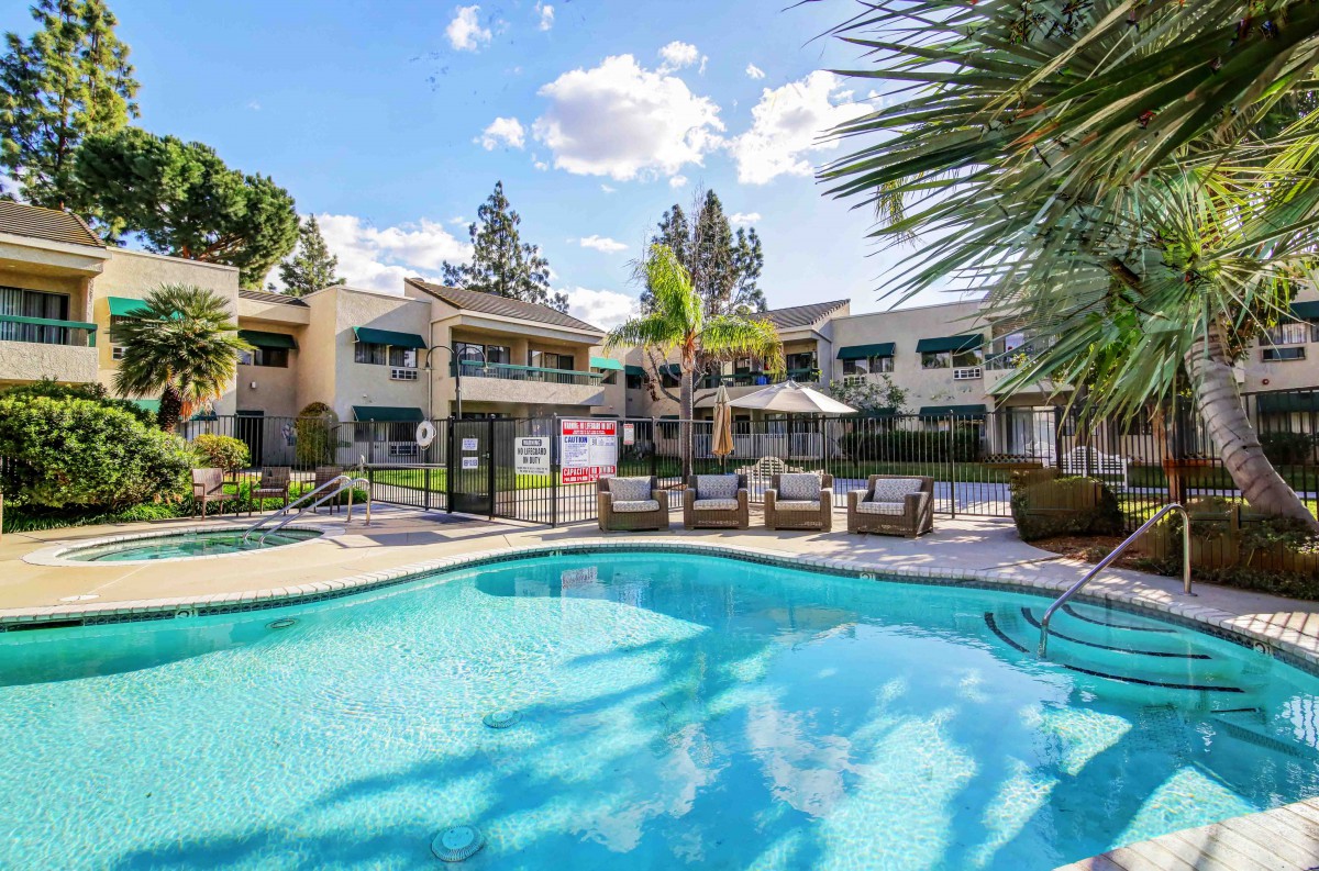 A sunny day at an apartment complex featuring a swimming pool and surrounded by lush greenery and palm trees.