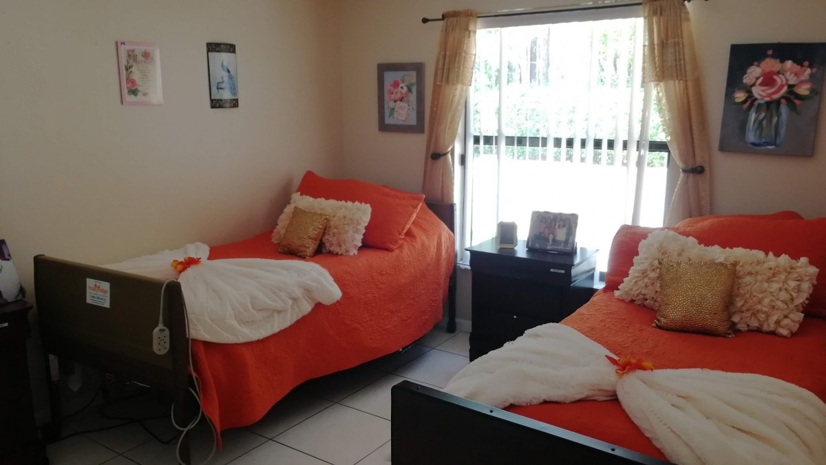A cozy bedroom with twin beds adorned in orange bedding and decorative pillows, featuring a large window with curtains and framed pictures on the walls.