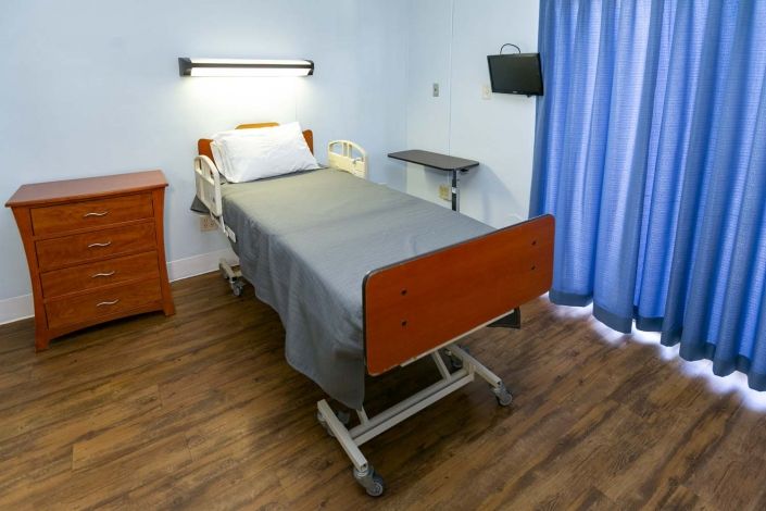 A hospital room featuring a single bed with gray linens, a bedside table, and a TV.