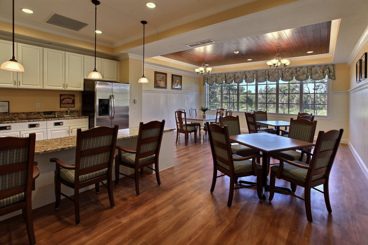 A modern dining and kitchen area with wooden flooring, featuring several tables and chairs under warm lighting.