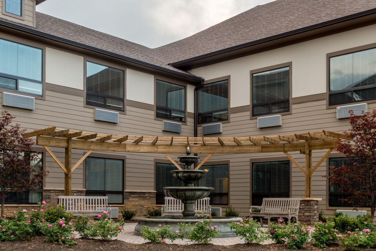 A peaceful courtyard with a fountain, pergola, and benches surrounded by a two-story building.