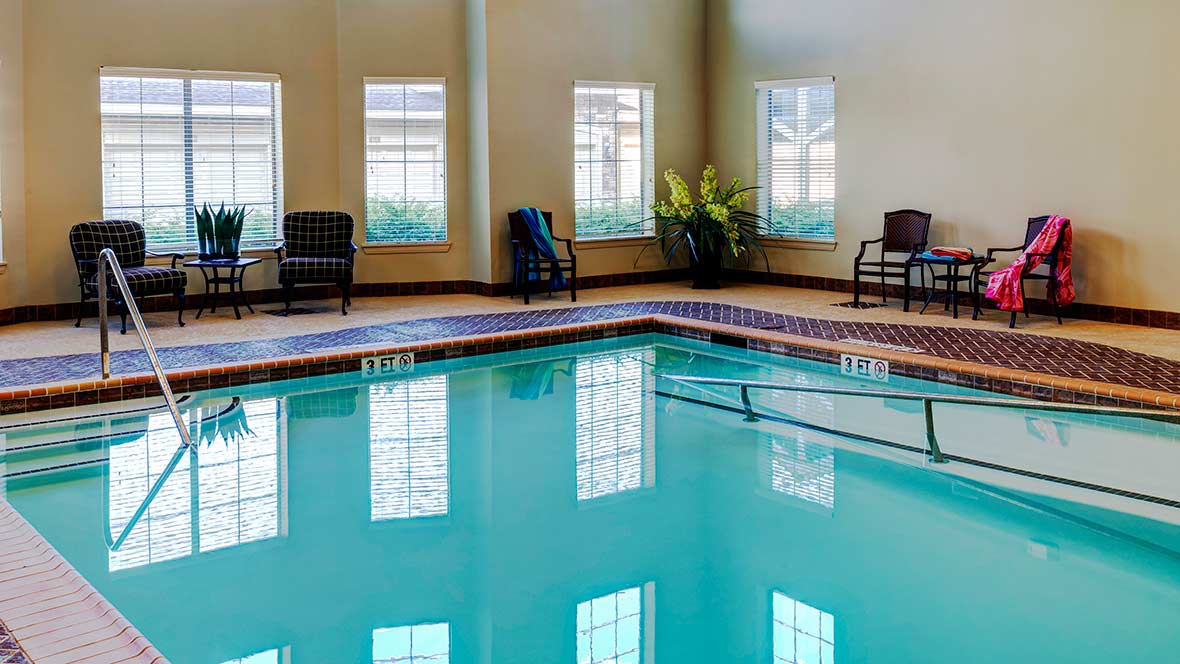 Indoor swimming pool with surrounding chairs and large windows.