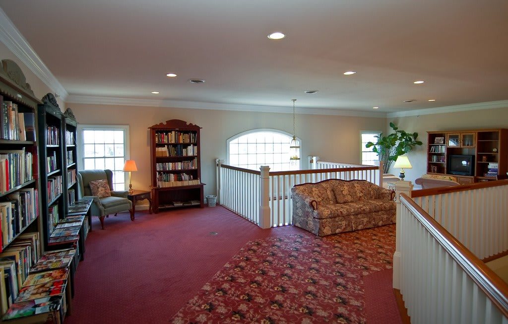 A cozy living area with a red carpet, featuring a sofa, bookshelf, and soft lighting.